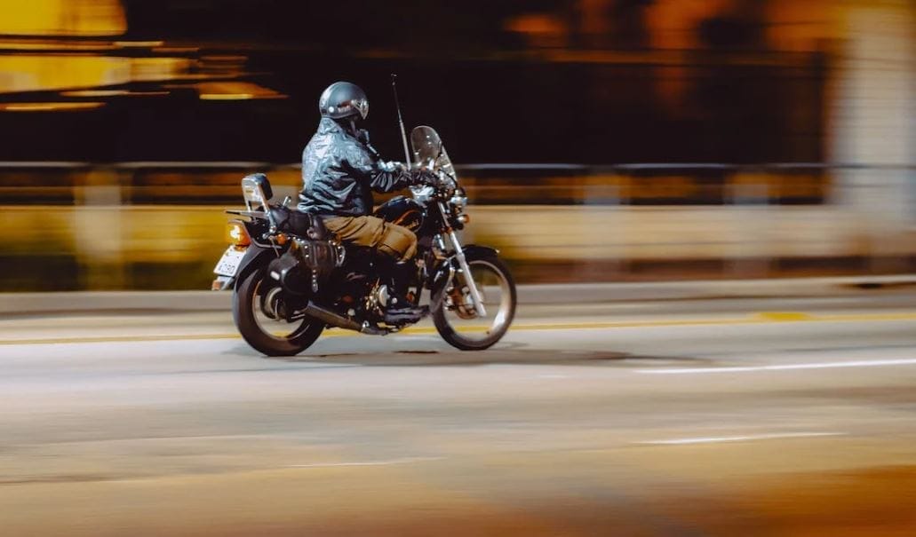 Unrecognizable biker riding motorcycle at night. Photo by Thgusstavo Santana via Pexels.